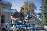 A person wearing safety equipment operates a cordless mitre saw at a construction site.