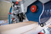 Cordless mitre saw cutting a wooden board in a workshop.