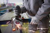 A person wearing safety equipment grinds a metal bar with a handheld angle grinder.