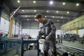A person wearing safety equipment grinds metal, sparks flying in a large industrial workshop.