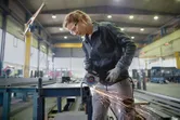 A person wearing safety equipment grinds metal on a workbench, producing sparks.