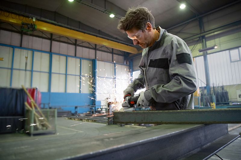 A person wearing safety equipment grinds metal with an angle grinder, sparks flying.