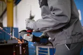 A person wearing safety equipment grinds metal, producing sparks in a workshop.