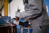 A person wearing safety equipment grinds metal, producing sparks in a workshop.