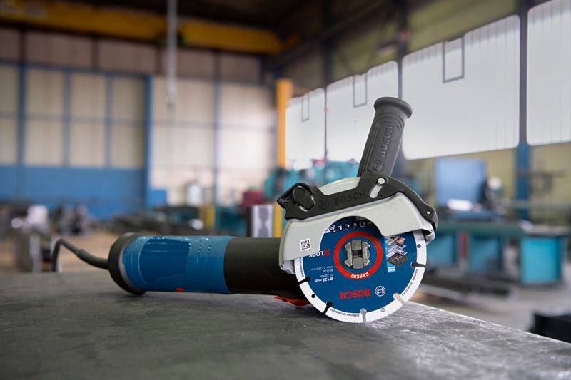 Angle grinder with X-LOCK system resting on a workbench in an industrial workshop.