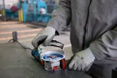 A person wearing safety equipment attaches a disc to an angle grinder on a workbench.