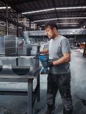 A person wearing safety equipment secures metal ductwork using a cordless rivet gun.