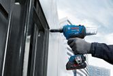 A person wearing safety equipment fastens a metal panel with a cordless rivet gun.