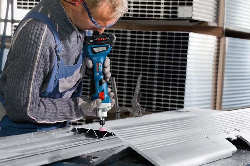A person wearing safety equipment grinds a metal sheet with a cordless straight grinder.