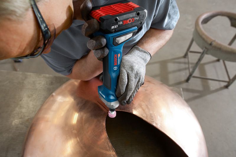 A person wearing safety equipment grinds the edge of a large metal dome.