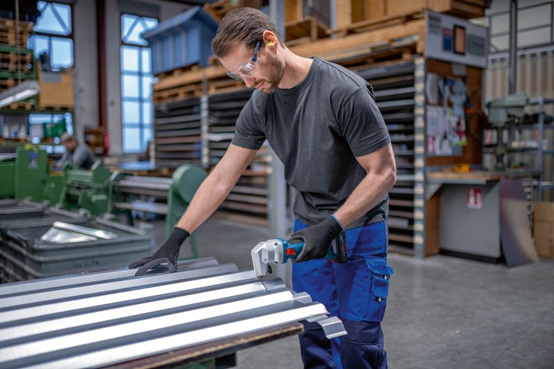 A person wearing safety equipment cuts sheet metal with a cordless nibbler in a workshop.
