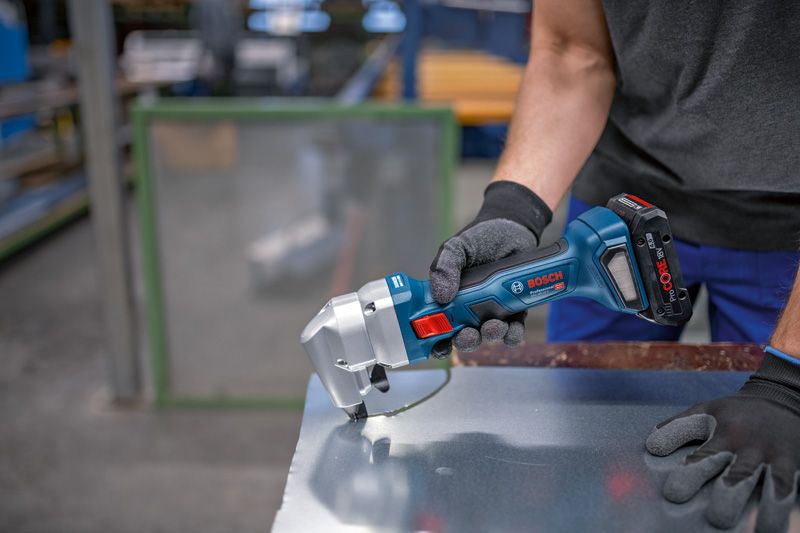 A person wearing safety equipment cuts sheet metal with a cordless nibbler.
