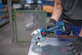 A person wearing safety equipment cuts sheet metal with a cordless nibbler.