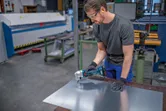 A person wearing safety equipment uses a cordless nibbler to cut sheet metal.