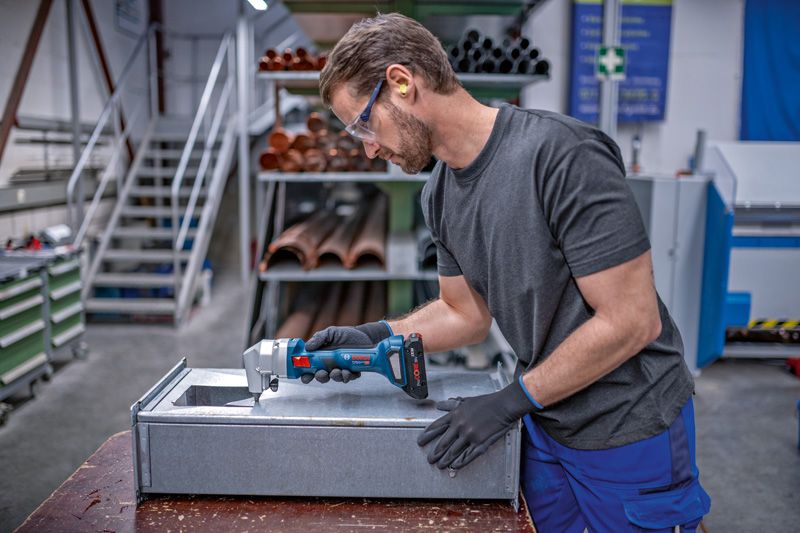 A person wearing safety equipment trims sheet metal with a cordless nibbler.
