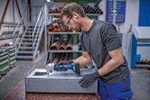 A person wearing safety equipment trims sheet metal with a cordless nibbler.