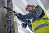 A person wearing safety equipment cuts a pipe with a reciprocating saw.