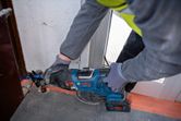 A person wearing safety equipment cuts metal using a cordless reciprocating saw.