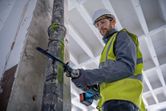 A person wearing safety equipment cuts a metal pipe with a reciprocating saw.