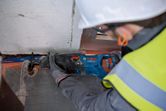 A person wearing safety equipment uses a reciprocating saw to cut a metal pipe.
