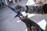 Person wearing safety equipment installs a reciprocating saw blade in an unfinished room.