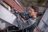 Person wearing safety equipment uses a reciprocating saw to cut roof wood outdoors.