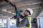 Person wearing safety equipment cuts a ceiling pipe with a reciprocating saw.