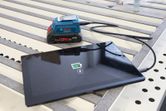 Tablet charging from a portable power bank using a USB cable on a workbench.
