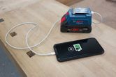 Portable charger connected to a smartphone charging on a wooden workbench.