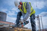 A person wearing safety equipment grinds rebar with a cordless angle grinder at a construction site.