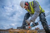 A person wearing safety equipment cuts rebar with a cordless angle grinder.