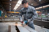 A person wearing safety equipment grinds metal, producing sparks in an industrial setting.