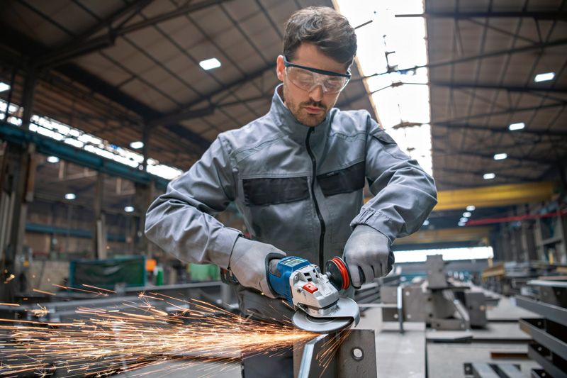 A person wearing safety equipment grinds metal, producing sparks in an industrial workshop.