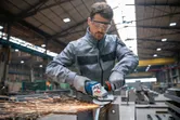 A person wearing safety equipment grinds metal, producing sparks in an industrial workshop.