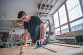Person wearing safety equipment sands a wooden door with a cordless orbital sander.
