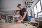 A person wearing safety equipment sands a wooden door with a cordless orbital sander.