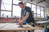 A person wearing safety equipment sands a wooden door with a cordless orbital sander.
