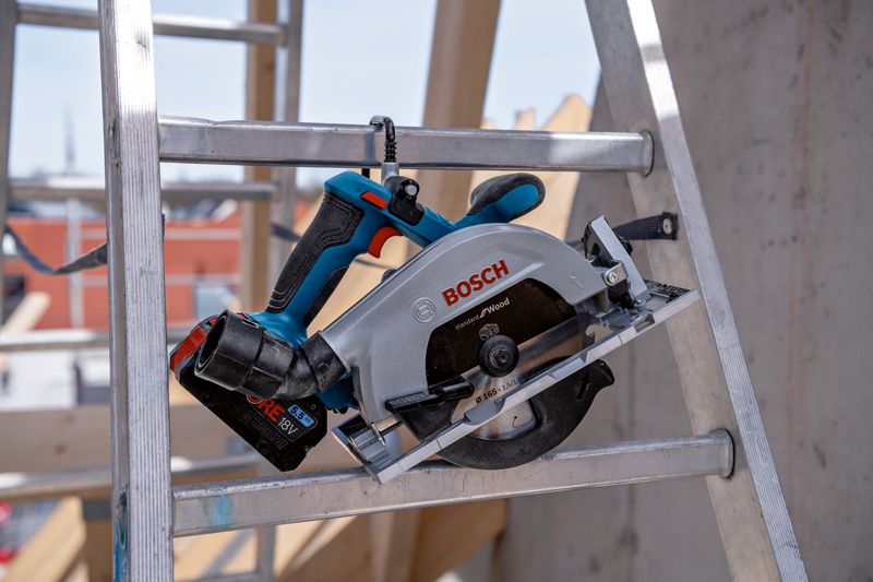 Cordless circular saw resting on a metal ladder at a construction site.