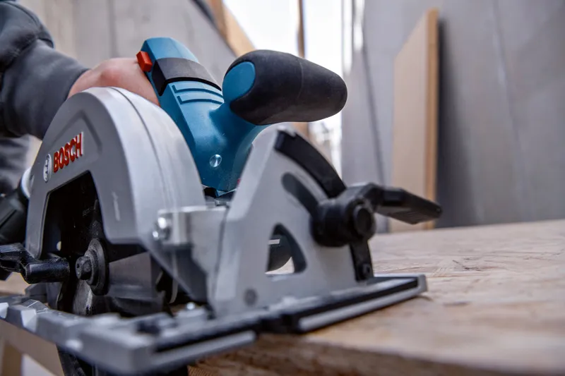 A person guides a circular saw along a wooden board in a workshop.