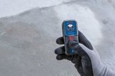 Person wearing safety equipment operates a compact laser measure on a concrete surface.