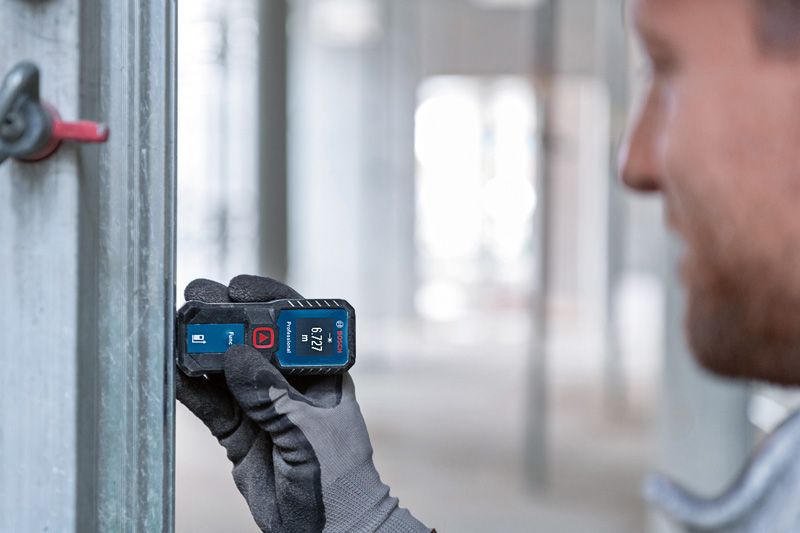 A person wearing safety equipment uses a laser measure to check distance on a metal frame.