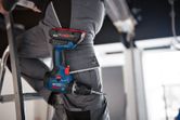 A person wearing safety equipment stands on a ladder with a cordless combi drill in their pocket.