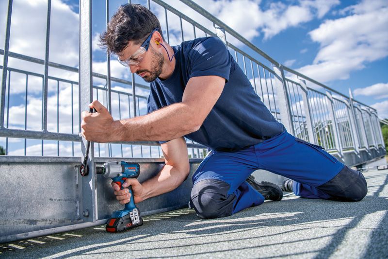 GDS 18V-450 HC A person wearing safety equipment fastens a metal fence with a cordless impact wrench.