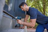 A person wearing safety equipment uses a cordless impact wrench to fasten bolts on a metal frame.