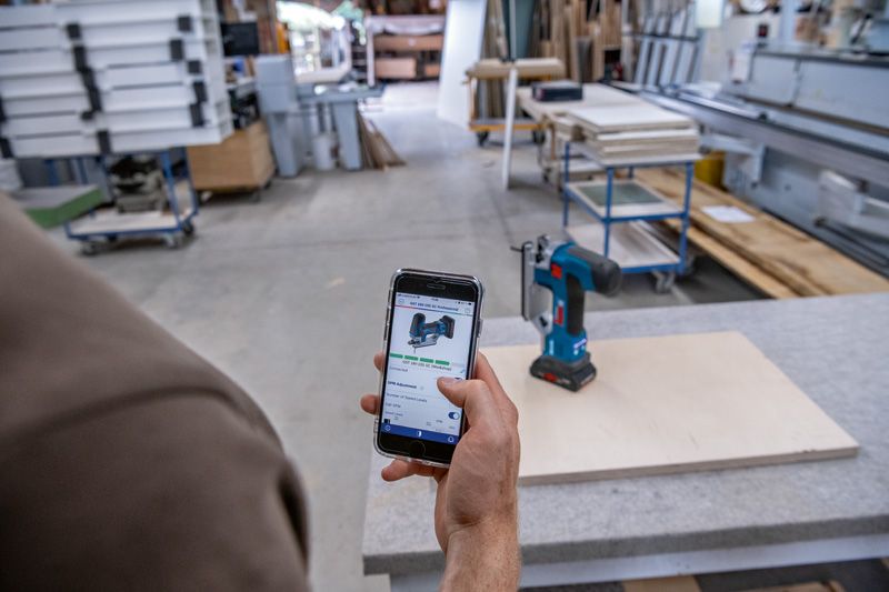 A person uses a smartphone to reference a cordless drill in a woodworking shop.