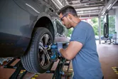 A person wearing safety equipment uses an impact wrench to tighten bolts on a car wheel.