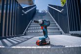 Cordless power drill placed on a metal grate at the bottom of outdoor stairs.