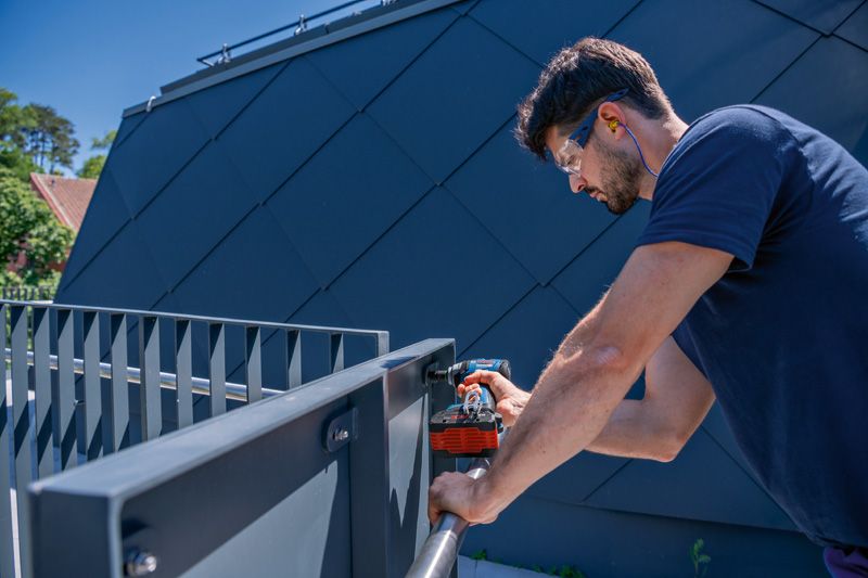 GDS 18V-330 HC A person wearing safety equipment drills into a metal railing outdoors.