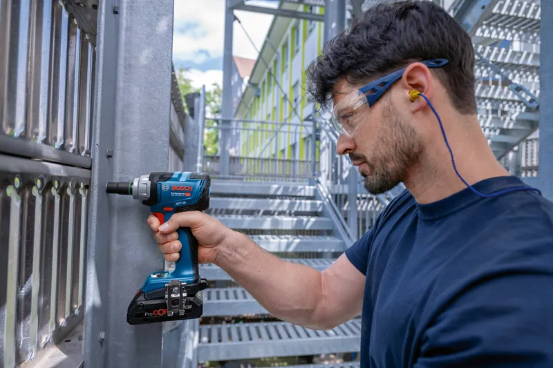GDS 18V-330 HC A person wearing safety equipment uses a cordless impact wrench on a metal structure.