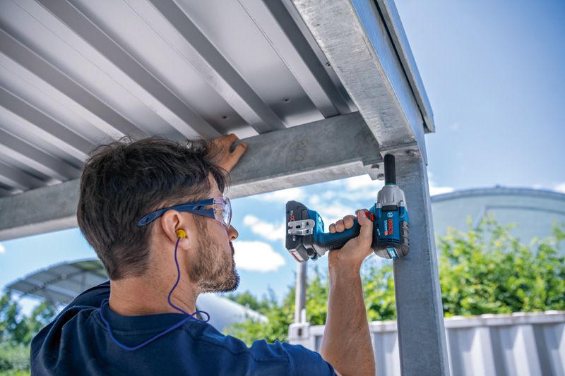 GDS 18V-450 HC A person wearing safety equipment uses an impact wrench on a metal structure.